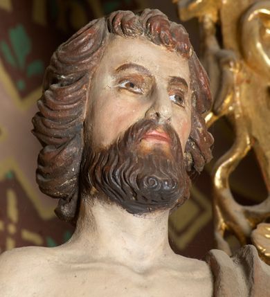 Zdjęcie nr 4: Rzeźba wolnostojąca, przedstawia św. Jana Chrzciciela, ustawiona na niskim, zielonym cokole na planie kwadratu. Święty ukazany frontalnie, w postawie stojącej z krzyżem o długim drzewcu w prawej dłoni oraz zamkniętą księgą w lewej. Twarz podłużna z długim i wąskim nosem, ze wzrokiem skierowanym w dal, okolona brązową, średniej długości brodą oraz krótkimi włosami, zasłaniającymi uszy.  Święty jest ubrany w szatę uszytą ze skóry zwierzęcej, odsłaniającą nagi tors i nogi poniżej kolan. Sylwetka szczupła. Polichromia w odsłoniętych partiach ciała naturalistyczna. 