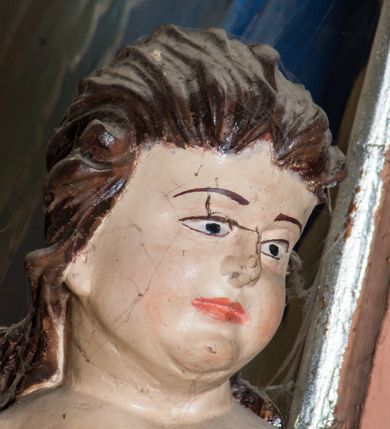 Zdjęcie nr 9: Krucyfiks zawieszony w łuku tęczowym kościoła. Do prostego krzyża przybita trzema gwoździami figura umarłego Chrystusa. Postać ukazana w dużym zwisie, o szeroko rozłożonych ramionach, z głową opadającą na prawy bark, nogi lekko ugięte w kolanach. Twarz Chrystusa jest podłużna, o zamkniętych oczach, długim i wąskim nosie, okolona jest krótką brodą rozdzieloną na końcu na dwa pukle i długimi włosami w postaci wijących się pukli, opadających na plecy i prawe ramię. Na głowie szeroka korona cierniowa, a wokół niej krzyżowy nimb promienisty. Ciało o wyraźnie podkreślonej anatomii, z silnie zaznaczoną muskulaturą. Perizonium przewieszone przez podwójny sznur, odsłaniające lewe biodro. Krzyż prosty, gładki, malowany na kolor ciemnobrązowy. Po lewej stronie krzyża nadlatujący aniołek, widoczny z lewego profilu, przepasany złotą tkaniną. Nad głową Chrystusa na pionowej belce banderola z napisem „I.N.R.I.” Polichromia w odsłoniętych partiach ciała naturalistyczna, szaty i detale złocone. 