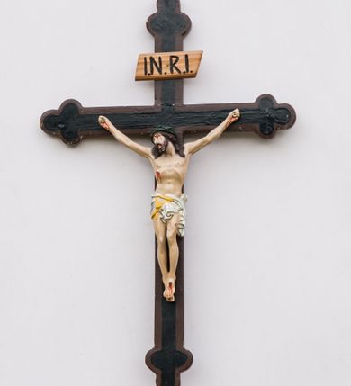 Zdjęcie nr 1: Krzyż procesyjny na długim drzewcu zwieńczonym kulą, na której zatknięty jest krucyfiks z rzeźbą Chrystusa. Chrystus ukazany jest w lekkim zwisie, przybity do krzyża trzema gwoździami, ze stopami założonymi lewa na prawą, nogami delikatnie ugiętymi w kolanach, z głową przechyloną na prawe ramię. Chrystus ma biodra ciasno oplecione białym perizonium, przewiązanym żółtym sznurem. Twarz podłużna, okolona krótką brodą; włosy długie i ciemnobrązowe, spływające do przodu na ramiona, na głowie zielona korona cierniowa, spod której spływają strużki krwi. Na dłoniach, stopach i boku widoczne krwawe rany po męce. Polichromia ciała naturalistyczna. Krzyż o ramionach zakończonych trójlistnie, malowany na czarno, obwiedziony ciemnobrązowym konturem na brzegach; nad głową Chrystusa wisi tabliczka z napisem „I.N.R.I.”
