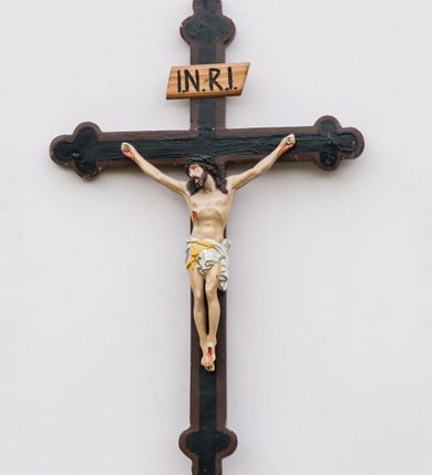 Zdjęcie nr 1: Krzyż procesyjny na długim drzewcu zwieńczonym kulą, na której zatknięty jest krucyfiks z rzeźbą Chrystusa. Chrystus ukazany jest w lekkim zwisie, przybity do krzyża trzema gwoździami, ze stopami założonymi lewa na prawą, nogami delikatnie ugiętymi w kolanach, z głową przechyloną na prawe ramię. Chrystus ma biodra ciasno oplecione białym perizonium, przewiązanym żółtym sznurem. Twarz podłużna, okolona krótką brodą; włosy długie i ciemnobrązowe, spływające do przodu na ramiona, na głowie zielona korona cierniowa, spod której spływają strużki krwi. Na dłoniach, stopach i boku widoczne krwawe rany po męce. Polichromia ciała naturalistyczna. Krzyż o ramionach zakończonych trójlistnie, malowany na czarno, obwiedziony ciemnobrązowym konturem na brzegach; nad głową Chrystusa wisi tabliczka z napisem „I.N.R.I.”
