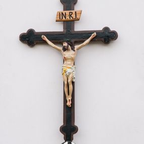 Zdjęcie nr 1: Krzyż procesyjny na długim drzewcu zwieńczonym kulą, na której zatknięty jest krucyfiks z rzeźbą Chrystusa. Chrystus ukazany jest w lekkim zwisie, przybity do krzyża trzema gwoździami, ze stopami założonymi lewa na prawą, nogami delikatnie ugiętymi w kolanach, z głową przechyloną na prawe ramię. Chrystus ma biodra ciasno oplecione białym perizonium, przewiązanym żółtym sznurem. Twarz podłużna, okolona krótką brodą; włosy długie i ciemnobrązowe, spływające do przodu na ramiona, na głowie zielona korona cierniowa, spod której spływają strużki krwi. Na dłoniach, stopach i boku widoczne krwawe rany po męce. Polichromia ciała naturalistyczna. Krzyż o ramionach zakończonych trójlistnie, malowany na czarno, obwiedziony ciemnobrązowym konturem na brzegach; nad głową Chrystusa wisi tabliczka z napisem „I.N.R.I.”

