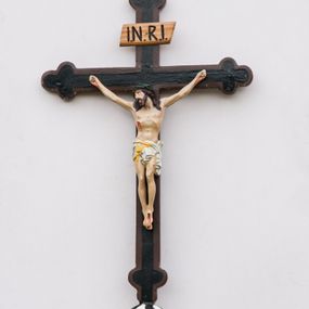Zdjęcie nr 1: Krzyż procesyjny na długim drzewcu zwieńczonym kulą, na której zatknięty jest krucyfiks z rzeźbą Chrystusa. Chrystus ukazany jest w lekkim zwisie, przybity do krzyża trzema gwoździami, ze stopami założonymi lewa na prawą, nogami delikatnie ugiętymi w kolanach, z głową przechyloną na prawe ramię. Chrystus ma biodra ciasno oplecione białym perizonium, przewiązanym żółtym sznurem. Twarz podłużna, okolona krótką brodą; włosy długie i ciemnobrązowe, spływające do przodu na ramiona, na głowie zielona korona cierniowa, spod której spływają strużki krwi. Na dłoniach, stopach i boku widoczne krwawe rany po męce. Polichromia ciała naturalistyczna. Krzyż o ramionach zakończonych trójlistnie, malowany na czarno, obwiedziony ciemnobrązowym konturem na brzegach; nad głową Chrystusa wisi tabliczka z napisem „I.N.R.I.”
