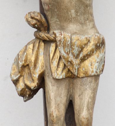 Zdjęcie nr 4: Rzeźba Chrystusa przybita do krzyża trzema gwoździami. Chrystus został ukazany w typie Cristo morte, w delikatnym zwisie, o szeroko rozłożonych ramionach, z głową skłonioną na prawe ramię, stopami założonymi prawa na lewą. Biodra ma przepasane złotym perizonium przewiązanym grubym sznurem, z jednym końcem zwisającym wzdłuż prawego uda, a powyżej tego fałdu ze sporym węzłem uformowanym z draperii powyżej sznura. Chrystus ma podłużną twarz, długi i wąski nos, zamknięte oczy, krótką brodę; włosy długie, ułożone w grube pukle, spływające na plecy i prawe ramię. Na głowie ma założoną szeroką koronę cierniową. Jego ciało jest szczupłe, o wyraźnie podkreślonej linii żeber, wąskiej talii. Nad głową Chrystusa umieszczona jest tabliczka z napisem „INRI” ujęta kartuszową ramą. Krzyż prosty, gładki, malowany na kolor ciemnobrązowy. Polichromia ciała naturalistyczna. Kartusz złocony i srebrzony.


 