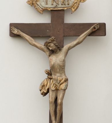 Zdjęcie nr 1: Rzeźba Chrystusa przybita do krzyża trzema gwoździami. Chrystus został ukazany w typie Cristo morte, w delikatnym zwisie, o szeroko rozłożonych ramionach, z głową skłonioną na prawe ramię, stopami założonymi prawa na lewą. Biodra ma przepasane złotym perizonium przewiązanym grubym sznurem, z jednym końcem zwisającym wzdłuż prawego uda, a powyżej tego fałdu ze sporym węzłem uformowanym z draperii powyżej sznura. Chrystus ma podłużną twarz, długi i wąski nos, zamknięte oczy, krótką brodę; włosy długie, ułożone w grube pukle, spływające na plecy i prawe ramię. Na głowie ma założoną szeroką koronę cierniową. Jego ciało jest szczupłe, o wyraźnie podkreślonej linii żeber, wąskiej talii. Nad głową Chrystusa umieszczona jest tabliczka z napisem „INRI” ujęta kartuszową ramą. Krzyż prosty, gładki, malowany na kolor ciemnobrązowy. Polichromia ciała naturalistyczna. Kartusz złocony i srebrzony.


 
