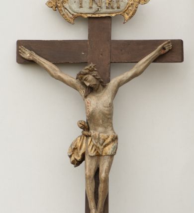 Zdjęcie nr 1: Rzeźba Chrystusa przybita do krzyża trzema gwoździami. Chrystus został ukazany w typie Cristo morte, w delikatnym zwisie, o szeroko rozłożonych ramionach, z głową skłonioną na prawe ramię, stopami założonymi prawa na lewą. Biodra ma przepasane złotym perizonium przewiązanym grubym sznurem, z jednym końcem zwisającym wzdłuż prawego uda, a powyżej tego fałdu ze sporym węzłem uformowanym z draperii powyżej sznura. Chrystus ma podłużną twarz, długi i wąski nos, zamknięte oczy, krótką brodę; włosy długie, ułożone w grube pukle, spływające na plecy i prawe ramię. Na głowie ma założoną szeroką koronę cierniową. Jego ciało jest szczupłe, o wyraźnie podkreślonej linii żeber, wąskiej talii. Nad głową Chrystusa umieszczona jest tabliczka z napisem „INRI” ujęta kartuszową ramą. Krzyż prosty, gładki, malowany na kolor ciemnobrązowy. Polichromia ciała naturalistyczna. Kartusz złocony i srebrzony.


 