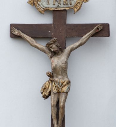 Zdjęcie nr 5: Rzeźba Chrystusa przybita do krzyża trzema gwoździami. Chrystus został ukazany w typie Cristo morte, w delikatnym zwisie, o szeroko rozłożonych ramionach, z głową skłonioną na prawe ramię, stopami założonymi prawa na lewą. Biodra ma przepasane złotym perizonium przewiązanym grubym sznurem, z jednym końcem zwisającym wzdłuż prawego uda, a powyżej tego fałdu ze sporym węzłem uformowanym z draperii powyżej sznura. Chrystus ma podłużną twarz, długi i wąski nos, zamknięte oczy, krótką brodę; włosy długie, ułożone w grube pukle, spływające na plecy i prawe ramię. Na głowie ma założoną szeroką koronę cierniową. Jego ciało jest szczupłe, o wyraźnie podkreślonej linii żeber, wąskiej talii. Nad głową Chrystusa umieszczona jest tabliczka z napisem „INRI” ujęta kartuszową ramą. Krzyż prosty, gładki, malowany na kolor ciemnobrązowy. Polichromia ciała naturalistyczna. Kartusz złocony i srebrzony.


 