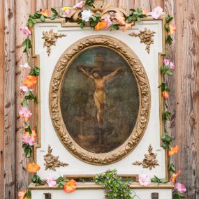 Zdjęcie nr 1: Feretron dwustronny z przedstawieniem Chrystusa Ukrzyżowanego oraz św. Izydora Oracza ustawiony na prostopadłościennym, zdwojonym cokole, zaopatrzonym w otwory na drążki do noszenia. Obrazy w kształcie owalu, ujęte prostokątną ramą z uszatymi narożami, w polu których płaskorzeźbione gałązki kwiatów. Rama wokół obrazu owalna, dekorowana drobnymi kwiatkami i opleciona karbowaną wstęgą. Zwieńczenie proste w formie stylizowanych liści akantu z zatkniętym u szczytu krzyżykiem łacińskim. Po jednej stronie feretronu obraz Ukrzyżowania Chrystusa. W centrum kompozycji ukazany krucyfiks z Chrystusem przybitym do krzyża trzema gwoździami, z głową przechyloną na prawe ramię. Wokół bioder białe perizonium. Na głowie korona cierniowa i kolisty nimb. Sylwetka szczupła, z poprawnie zaznaczoną anatomią. Nad głową Chrystusa tabliczka z tytułem winy: „INRI”. Po lewej stronie obrazu Matka Boska oraz św. Jan Ewangelista ukazani w postawie stojącej, zwróceni w stronę krzyża. U stóp krzyża wąż. Pozostałe elementy nieczytelne z powodu znacznego zniszczenia obrazu. Po drugiej stronie feretronu przedstawiono św. Izydora Oracza. Święty Izydor ukazany w pozycji klęczącej przed kapliczką, zwrócony delikatnie trzy czwarte w swoją prawą stronę, ze skrzyżowanymi na piersi dłońmi. Ubrany w rozpięty żupan przewiązany pasem, pod spodem biała i długa koszula. Twarz szeroka, włosy sięgające do ramion, z grzywką. Po prawej stronie kompozycji, w tle anioł orzący pole. Kapliczka ustawiona na zdwojonym, wysokim cokole podtrzymującym zabudowaną niszę, w której umieszczony krucyfiks. U kolan świętego kapelusz i kij. Tło jasne, w górnej części błękitne niebo. Struktura feretronu polichromowana na biało, detale i ornamemtyka złocone. 