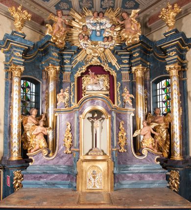 Zdjęcie nr 1: Nastawa ołtarzowa architektoniczna, trójosiowa, jednokondygnacyjna, ustawiona na wysokim cokole. Ołtarz wolnostojący, odsunięty od retabulum, drewniany, sarkofagowy z drewnianą mensą, na nim ustawione tabernakulum. Nastawa opasująca trójbocznie zamknięte prezbiterium, osie wydzielone czterema parami pilastrów o trzonach dekorowanych rocaille'em, przed którymi stoją cztery kolumny o kapitelach kompozytowych i trzonach z dekoracją geometryczną, dźwigających imposty. W polu środkowym nisza w formie stojącego prostokąta zamkniętego łukiem segmentowym nadwieszonym z uskokiem, ujęta profilowaną ramą dekorowaną rocaille'em z dużo mniejszym obrazem Matki Boskiej Nieustającej Pomocy w osobnej ramie na czerwonym tle. Osie boczne przeprute oknami w formie stojącego prostokąta zamkniętego łukiem segmentowym, na ich tle stoją figury aniołów. Nad polem głównym medalion z obłoków i uskrzydlonych główek anielskich z gołębicą Ducha Świętego w glorii promienistej. Na belkowaniu, na osi wewnętrznych impostów dwa siedzące na obłokach putta, na osi zewnętrznych rokokowe wazony. Nastawa flankowana dwoma przyściennymi cokołami, na których stoją figury św. Piotra i św. Pawła. Struktura architektoniczna polichromowana na sposób imitujący niebiesko-białą marmoryzację, trzony pilastrów fioletową. Ornamentyka, profile, kolumny i gloria pozłacane i posrebrzane. 
 





