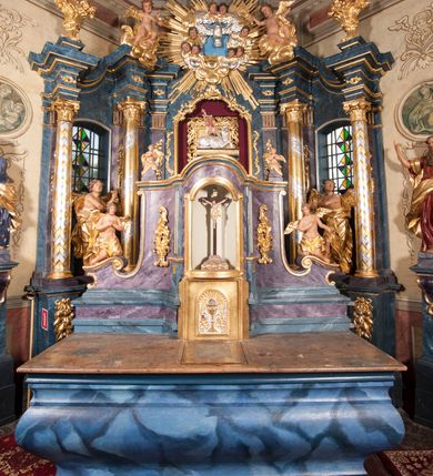 Zdjęcie nr 27: Nastawa ołtarzowa architektoniczna, trójosiowa, jednokondygnacyjna, ustawiona na wysokim cokole. Ołtarz wolnostojący, odsunięty od retabulum, drewniany, sarkofagowy z drewnianą mensą, na nim ustawione tabernakulum. Nastawa opasująca trójbocznie zamknięte prezbiterium, osie wydzielone czterema parami pilastrów o trzonach dekorowanych rocaille&#039;em, przed którymi stoją cztery kolumny o kapitelach kompozytowych i trzonach z dekoracją geometryczną, dźwigających imposty. W polu środkowym nisza w formie stojącego prostokąta zamkniętego łukiem segmentowym nadwieszonym z uskokiem, ujęta profilowaną ramą dekorowaną rocaille&#039;em z dużo mniejszym obrazem Matki Boskiej Nieustającej Pomocy w osobnej ramie na czerwonym tle. Osie boczne przeprute oknami w formie stojącego prostokąta zamkniętego łukiem segmentowym, na ich tle stoją figury aniołów. Nad polem głównym medalion z obłoków i uskrzydlonych główek anielskich z gołębicą Ducha Świętego w glorii promienistej. Na belkowaniu, na osi wewnętrznych impostów dwa siedzące na obłokach putta, na osi zewnętrznych rokokowe wazony. Nastawa flankowana dwoma przyściennymi cokołami, na których stoją figury św. Piotra i św. Pawła. Struktura architektoniczna polichromowana na sposób imitujący niebiesko-białą marmoryzację, trzony pilastrów fioletową. Ornamentyka, profile, kolumny i gloria pozłacane i posrebrzane. 
 





