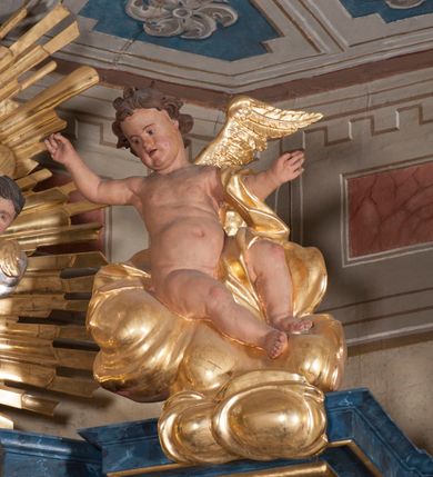 Zdjęcie nr 5: Nastawa ołtarzowa architektoniczna, trójosiowa, jednokondygnacyjna, ustawiona na wysokim cokole. Ołtarz wolnostojący, odsunięty od retabulum, drewniany, sarkofagowy z drewnianą mensą, na nim ustawione tabernakulum. Nastawa opasująca trójbocznie zamknięte prezbiterium, osie wydzielone czterema parami pilastrów o trzonach dekorowanych rocaille'em, przed którymi stoją cztery kolumny o kapitelach kompozytowych i trzonach z dekoracją geometryczną, dźwigających imposty. W polu środkowym nisza w formie stojącego prostokąta zamkniętego łukiem segmentowym nadwieszonym z uskokiem, ujęta profilowaną ramą dekorowaną rocaille'em z dużo mniejszym obrazem Matki Boskiej Nieustającej Pomocy w osobnej ramie na czerwonym tle. Osie boczne przeprute oknami w formie stojącego prostokąta zamkniętego łukiem segmentowym, na ich tle stoją figury aniołów. Nad polem głównym medalion z obłoków i uskrzydlonych główek anielskich z gołębicą Ducha Świętego w glorii promienistej. Na belkowaniu, na osi wewnętrznych impostów dwa siedzące na obłokach putta, na osi zewnętrznych rokokowe wazony. Nastawa flankowana dwoma przyściennymi cokołami, na których stoją figury św. Piotra i św. Pawła. Struktura architektoniczna polichromowana na sposób imitujący niebiesko-białą marmoryzację, trzony pilastrów fioletową. Ornamentyka, profile, kolumny i gloria pozłacane i posrebrzane. 
 





