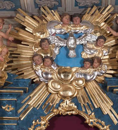 Zdjęcie nr 30: Nastawa ołtarzowa architektoniczna, trójosiowa, jednokondygnacyjna, ustawiona na wysokim cokole. Ołtarz wolnostojący, odsunięty od retabulum, drewniany, sarkofagowy z drewnianą mensą, na nim ustawione tabernakulum. Nastawa opasująca trójbocznie zamknięte prezbiterium, osie wydzielone czterema parami pilastrów o trzonach dekorowanych rocaille&#039;em, przed którymi stoją cztery kolumny o kapitelach kompozytowych i trzonach z dekoracją geometryczną, dźwigających imposty. W polu środkowym nisza w formie stojącego prostokąta zamkniętego łukiem segmentowym nadwieszonym z uskokiem, ujęta profilowaną ramą dekorowaną rocaille&#039;em z dużo mniejszym obrazem Matki Boskiej Nieustającej Pomocy w osobnej ramie na czerwonym tle. Osie boczne przeprute oknami w formie stojącego prostokąta zamkniętego łukiem segmentowym, na ich tle stoją figury aniołów. Nad polem głównym medalion z obłoków i uskrzydlonych główek anielskich z gołębicą Ducha Świętego w glorii promienistej. Na belkowaniu, na osi wewnętrznych impostów dwa siedzące na obłokach putta, na osi zewnętrznych rokokowe wazony. Nastawa flankowana dwoma przyściennymi cokołami, na których stoją figury św. Piotra i św. Pawła. Struktura architektoniczna polichromowana na sposób imitujący niebiesko-białą marmoryzację, trzony pilastrów fioletową. Ornamentyka, profile, kolumny i gloria pozłacane i posrebrzane. 
 





