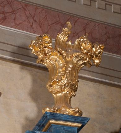 Zdjęcie nr 22: Nastawa ołtarzowa architektoniczna, trójosiowa, jednokondygnacyjna, ustawiona na wysokim cokole. Ołtarz wolnostojący, odsunięty od retabulum, drewniany, sarkofagowy z drewnianą mensą, na nim ustawione tabernakulum. Nastawa opasująca trójbocznie zamknięte prezbiterium, osie wydzielone czterema parami pilastrów o trzonach dekorowanych rocaille&#039;em, przed którymi stoją cztery kolumny o kapitelach kompozytowych i trzonach z dekoracją geometryczną, dźwigających imposty. W polu środkowym nisza w formie stojącego prostokąta zamkniętego łukiem segmentowym nadwieszonym z uskokiem, ujęta profilowaną ramą dekorowaną rocaille&#039;em z dużo mniejszym obrazem Matki Boskiej Nieustającej Pomocy w osobnej ramie na czerwonym tle. Osie boczne przeprute oknami w formie stojącego prostokąta zamkniętego łukiem segmentowym, na ich tle stoją figury aniołów. Nad polem głównym medalion z obłoków i uskrzydlonych główek anielskich z gołębicą Ducha Świętego w glorii promienistej. Na belkowaniu, na osi wewnętrznych impostów dwa siedzące na obłokach putta, na osi zewnętrznych rokokowe wazony. Nastawa flankowana dwoma przyściennymi cokołami, na których stoją figury św. Piotra i św. Pawła. Struktura architektoniczna polichromowana na sposób imitujący niebiesko-białą marmoryzację, trzony pilastrów fioletową. Ornamentyka, profile, kolumny i gloria pozłacane i posrebrzane. 
 





