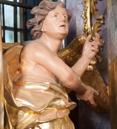 Zdjęcie nr 12: Nastawa ołtarzowa architektoniczna, trójosiowa, jednokondygnacyjna, ustawiona na wysokim cokole. Ołtarz wolnostojący, odsunięty od retabulum, drewniany, sarkofagowy z drewnianą mensą, na nim ustawione tabernakulum. Nastawa opasująca trójbocznie zamknięte prezbiterium, osie wydzielone czterema parami pilastrów o trzonach dekorowanych rocaille'em, przed którymi stoją cztery kolumny o kapitelach kompozytowych i trzonach z dekoracją geometryczną, dźwigających imposty. W polu środkowym nisza w formie stojącego prostokąta zamkniętego łukiem segmentowym nadwieszonym z uskokiem, ujęta profilowaną ramą dekorowaną rocaille'em z dużo mniejszym obrazem Matki Boskiej Nieustającej Pomocy w osobnej ramie na czerwonym tle. Osie boczne przeprute oknami w formie stojącego prostokąta zamkniętego łukiem segmentowym, na ich tle stoją figury aniołów. Nad polem głównym medalion z obłoków i uskrzydlonych główek anielskich z gołębicą Ducha Świętego w glorii promienistej. Na belkowaniu, na osi wewnętrznych impostów dwa siedzące na obłokach putta, na osi zewnętrznych rokokowe wazony. Nastawa flankowana dwoma przyściennymi cokołami, na których stoją figury św. Piotra i św. Pawła. Struktura architektoniczna polichromowana na sposób imitujący niebiesko-białą marmoryzację, trzony pilastrów fioletową. Ornamentyka, profile, kolumny i gloria pozłacane i posrebrzane. 
 





