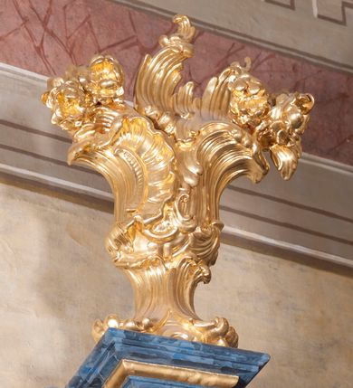 Zdjęcie nr 23: Nastawa ołtarzowa architektoniczna, trójosiowa, jednokondygnacyjna, ustawiona na wysokim cokole. Ołtarz wolnostojący, odsunięty od retabulum, drewniany, sarkofagowy z drewnianą mensą, na nim ustawione tabernakulum. Nastawa opasująca trójbocznie zamknięte prezbiterium, osie wydzielone czterema parami pilastrów o trzonach dekorowanych rocaille'em, przed którymi stoją cztery kolumny o kapitelach kompozytowych i trzonach z dekoracją geometryczną, dźwigających imposty. W polu środkowym nisza w formie stojącego prostokąta zamkniętego łukiem segmentowym nadwieszonym z uskokiem, ujęta profilowaną ramą dekorowaną rocaille'em z dużo mniejszym obrazem Matki Boskiej Nieustającej Pomocy w osobnej ramie na czerwonym tle. Osie boczne przeprute oknami w formie stojącego prostokąta zamkniętego łukiem segmentowym, na ich tle stoją figury aniołów. Nad polem głównym medalion z obłoków i uskrzydlonych główek anielskich z gołębicą Ducha Świętego w glorii promienistej. Na belkowaniu, na osi wewnętrznych impostów dwa siedzące na obłokach putta, na osi zewnętrznych rokokowe wazony. Nastawa flankowana dwoma przyściennymi cokołami, na których stoją figury św. Piotra i św. Pawła. Struktura architektoniczna polichromowana na sposób imitujący niebiesko-białą marmoryzację, trzony pilastrów fioletową. Ornamentyka, profile, kolumny i gloria pozłacane i posrebrzane. 
 





