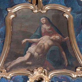 Zdjęcie nr 1: Obraz w formie zbliżonej do kwadratu, zamknięty faliście, o wklęsłych bokach i podstawie. W centrum przedstawienie siedzącej Marii, na której kolanach leży martwe ciało Chrystusa. Marka Boska zwrócona w trzech czwartych w prawo, z uniesioną głową, prawą ręką podtrzymuje rękę Chrystusa, lewą wyciąga w bok. Twarz okrągła, z migdałowatymi oczami skierowanymi ku górze, z których kapią łzy, o prostym nosie i pełnych ustach. Ubrana jest w czerwoną suknię, białą podwikę oraz niebieski płaszcz zarzucony na głowę i ramiona, opadający na jej lewą nogę. Ciało Chrystusa spoczywa na lewym kolanie Marii, z którego osuwa się na ziemię. Ukazane jest frontalnie, z głową opadającą na lewy bark oraz rozłożonymi na boki rękoma i skrzyżowanymi nogami. Twarz Chrystusa pociągła, o zamkniętych oczach i prostym nosie, okolona jasną, krótką brodą i włosami opadającymi na tył głowy. Ciało szczupłe z zaznaczonymi śladami męki. Biodra ma przesłonięte białym, krótkim perizonium. Po prawej stronie Marii leży korona cierniowa. Postacie ukazane na ciemnym tle pejzażu z widocznym po prawej stronie wzgórzem Golgoty z trzema krzyżami.

