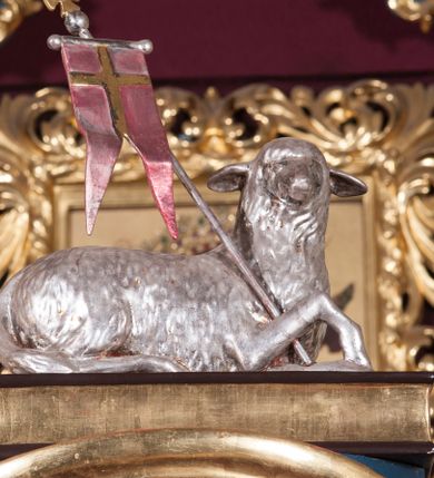 Zdjęcie nr 4: Tabernakulum w formie pozłoconej, prostopadłościennej skrzynki z metalowymi, pozłoconymi i posrebrzonymi drzwiczkami w kształcie stojącego prostokąta zamkniętego łukiem półkolistym z symbolami eucharystycznymi – kielichem z hostią, kłosami zbóż i winnym gronem. Nad tabernakulum tron wystawienia w formie obrotowej niszy o wypukłym licu w architektonicznej obudowie, ujęty spływami wolutowymi, na których znajdują się klęczące figury aniołów, opadającymi na profilowany cokół flankujący tabernakulum. Obrotowa nisza ujęta ramą, flankowana parą pilastrów dźwigających gzyms w formie łuku półkolistego, ujęta ornamentem roślinnym. Pośrodku na gzymsie baranek apokaliptyczny leżący na księdze, na krawędziach gzymsu na cokolikach dwie niewielkie figurki adorujących aniołków. Struktura polichromowana w sposób naśladujący marmoryzację w kolorze fioletowym, z niebieskimi detalami, tabernakulum pozłocone i posrebrzone, ornamentyka i profile pozłocone, figury o naturalnej karnacji i pozłoconych szatach. 

