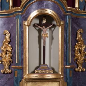 Zdjęcie nr 1: Tabernakulum w formie pozłoconej, prostopadłościennej skrzynki z metalowymi, pozłoconymi i posrebrzonymi drzwiczkami w kształcie stojącego prostokąta zamkniętego łukiem półkolistym z symbolami eucharystycznymi – kielichem z hostią, kłosami zbóż i winnym gronem. Nad tabernakulum tron wystawienia w formie obrotowej niszy o wypukłym licu w architektonicznej obudowie, ujęty spływami wolutowymi, na których znajdują się klęczące figury aniołów, opadającymi na profilowany cokół flankujący tabernakulum. Obrotowa nisza ujęta ramą, flankowana parą pilastrów dźwigających gzyms w formie łuku półkolistego, ujęta ornamentem roślinnym. Pośrodku na gzymsie baranek apokaliptyczny leżący na księdze, na krawędziach gzymsu na cokolikach dwie niewielkie figurki adorujących aniołków. Struktura polichromowana w sposób naśladujący marmoryzację w kolorze fioletowym, z niebieskimi detalami, tabernakulum pozłocone i posrebrzone, ornamentyka i profile pozłocone, figury o naturalnej karnacji i pozłoconych szatach. 

