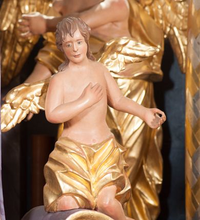 Zdjęcie nr 10: Tabernakulum w formie pozłoconej, prostopadłościennej skrzynki z metalowymi, pozłoconymi i posrebrzonymi drzwiczkami w kształcie stojącego prostokąta zamkniętego łukiem półkolistym z symbolami eucharystycznymi – kielichem z hostią, kłosami zbóż i winnym gronem. Nad tabernakulum tron wystawienia w formie obrotowej niszy o wypukłym licu w architektonicznej obudowie, ujęty spływami wolutowymi, na których znajdują się klęczące figury aniołów, opadającymi na profilowany cokół flankujący tabernakulum. Obrotowa nisza ujęta ramą, flankowana parą pilastrów dźwigających gzyms w formie łuku półkolistego, ujęta ornamentem roślinnym. Pośrodku na gzymsie baranek apokaliptyczny leżący na księdze, na krawędziach gzymsu na cokolikach dwie niewielkie figurki adorujących aniołków. Struktura polichromowana w sposób naśladujący marmoryzację w kolorze fioletowym, z niebieskimi detalami, tabernakulum pozłocone i posrebrzone, ornamentyka i profile pozłocone, figury o naturalnej karnacji i pozłoconych szatach. 

