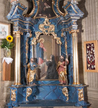 Zdjęcie nr 3: Obraz w formie stojącego prostokąta, przedstawiający św. Małgorzatę modlącą się przed Chrystusem z gorejącym sercem stojącym przed nią na obłoku. W prawym dolnym rogu obrazu klęcząca święta ukazana z profilu, zwrócona w prawo, z uniesioną głową i dłońmi złożonymi w geście modlitwy. Ubrana jest w czarny habit wizytki, z białym kapturem i czarnym welonem. Chrystus ukazany w lewym, górnym rogu, zwrócony w trzech czwartych w lewo, z pochylona głową. Prawą ręka wskazuje na znajdujące się na jego piersi gorejące serce, lewą wyciąga przed siebie. Twarz ma szczupłą, okoloną jasnym zarostem i jasnymi włosami opadającymi na ramiona. Ubrany jest w różową tunikę oraz niebieski płaszcz zarzucony na prawe ramię i opasujący go w talii. Scena ukazana jest we wnętrzu kościelnym, z widocznymi po prawej stronie kolumnami oraz arkadą wspartą na zdwojonych pilastrach doryckich i ołtarzem, nad którym unosi się postać Chrystusa.
