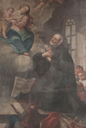 Zdjęcie nr 1: Obraz w formie stojącego prostokąta. W centrum obrazu św. Józef Kalasanty klęczący przed unoszącą się pośród obłoków Matką Boską z Dzieciątkiem. Święty zwrócony jest w trzech czwartych w prawo, z uniesioną głową i skrzyżowanymi na piersi rękami, w których trzyma gorejące serce i gałązkę lilii. Twarz ma pociągłą, o migdałowatych, wąskich oczach i lekko garbatym nosie, okoloną krótką, siwą brodą i włosami po bokach głowy, na jej czubku łysina. Ubrany jest w czarny habit zapinany z przodu na guziki, z białą koloratką oraz czarny płaszcz zarzucony na plecy. Przed nim leży czarny biret i otwarta księga z napisem „Consti/tutio/nes Cler[i]c[orum] / Regular[um] / Piarum / Schola/rum”. Na pierwszym planie ukazany od tyłu, w pozycji półleżącej, chłopiec z otwartą księgą. Obok, w prawym dolnym rogu na księgach leżą czerwony kapelusz kardynalski, pastorał i laska zakończona krzyżem arcybiskupim. W lewej, górnej części obrazu Matka Boska siedzi na obłoku, zwrócona jest w trzech czwartych w lewo, pochylona, obiema rękami trzyma stojące po jej prawej stronie Dzieciątko. Twarz o łagodnych rysach, wąskich oczach, okolona jasnymi włosami. Ubrana jest w jasnoróżową suknię z białą podwiką, niebieski płaszcz narzucony na kolana oraz jasnoróżowy, rozwiany welon na głowie. Dzieciątko zwrócone w trzech czwartych w lewo, z uniesioną prawą ręką w geście błogosławieństwa, przepasane w partii bioder białą tkaniną. U góry obrazu, pośród obłoków dwa putta. W prawej części obrazu, za świętym widoczne dwie postacie klęczących dzieci, spośród których jedno czyta księgę a drugie się modli. Scena ukazana we wnętrzu z widocznymi w tle pilastem i oknem. 
