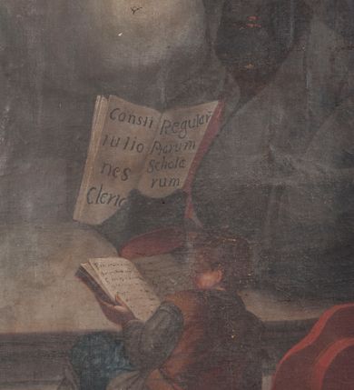 Zdjęcie nr 6: Obraz w formie stojącego prostokąta. W centrum obrazu św. Józef Kalasanty klęczący przed unoszącą się pośród obłoków Matką Boską z Dzieciątkiem. Święty zwrócony jest w trzech czwartych w prawo, z uniesioną głową i skrzyżowanymi na piersi rękami, w których trzyma gorejące serce i gałązkę lilii. Twarz ma pociągłą, o migdałowatych, wąskich oczach i lekko garbatym nosie, okoloną krótką, siwą brodą i włosami po bokach głowy, na jej czubku łysina. Ubrany jest w czarny habit zapinany z przodu na guziki, z białą koloratką oraz czarny płaszcz zarzucony na plecy. Przed nim leży czarny biret i otwarta księga z napisem „Consti/tutio/nes Cler[i]c[orum] / Regular[um] / Piarum / Schola/rum”. Na pierwszym planie ukazany od tyłu, w pozycji półleżącej, chłopiec z otwartą księgą. Obok, w prawym dolnym rogu na księgach leżą czerwony kapelusz kardynalski, pastorał i laska zakończona krzyżem arcybiskupim. W lewej, górnej części obrazu Matka Boska siedzi na obłoku, zwrócona jest w trzech czwartych w lewo, pochylona, obiema rękami trzyma stojące po jej prawej stronie Dzieciątko. Twarz o łagodnych rysach, wąskich oczach, okolona jasnymi włosami. Ubrana jest w jasnoróżową suknię z białą podwiką, niebieski płaszcz narzucony na kolana oraz jasnoróżowy, rozwiany welon na głowie. Dzieciątko zwrócone w trzech czwartych w lewo, z uniesioną prawą ręką w geście błogosławieństwa, przepasane w partii bioder białą tkaniną. U góry obrazu, pośród obłoków dwa putta. W prawej części obrazu, za świętym widoczne dwie postacie klęczących dzieci, spośród których jedno czyta księgę a drugie się modli. Scena ukazana we wnętrzu z widocznymi w tle pilastem i oknem. 
