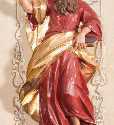 Zdjęcie nr 1: Rzeźba ustawiona na niskiej podstawie przedstawia św. Pawła, który został ukazany frontalnie, w kontrapoście. Lewą ręką podtrzymuje z przodu połę płaszcza i trzyma zamkniętą księgę, prawą unosi do góry z wyciągniętym wskazującym palcem. Twarz pociągła, o blisko siebie usytuowanych oczach, lekko garbatym nosie  i rozchylonych ustach, okolona długą, kręconą brodą opadającą na pierś oraz krótkimi kręconymi włosami. Święty ubrany jest w czerwoną tunikę przylegającą do ciała z szerokimi rękawami, przepasaną w talii o pozłacanym wzorze oraz płaszcz przewiązany diagonalnie przez biodra i zawieszony na prawym przedramieniu. Polichromia ciała naturalistyczna. 


