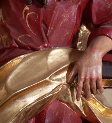 Zdjęcie nr 4: Rzeźba ustawiona na niskiej podstawie przedstawia św. Pawła, który został ukazany frontalnie, w kontrapoście. Lewą ręką podtrzymuje z przodu połę płaszcza i trzyma zamkniętą księgę, prawą unosi do góry z wyciągniętym wskazującym palcem. Twarz pociągła, o blisko siebie usytuowanych oczach, lekko garbatym nosie  i rozchylonych ustach, okolona długą, kręconą brodą opadającą na pierś oraz krótkimi kręconymi włosami. Święty ubrany jest w czerwoną tunikę przylegającą do ciała z szerokimi rękawami, przepasaną w talii o pozłacanym wzorze oraz płaszcz przewiązany diagonalnie przez biodra i zawieszony na prawym przedramieniu. Polichromia ciała naturalistyczna. 


