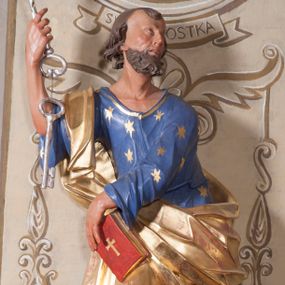 Zdjęcie nr 1: Figura ustawiona na niewielkiej podstawie. Zwrócona jest frontalnie, z uniesioną głową skierowaną w lewo, w kontrapoście, o esowato wygiętej sylwetce. Obie ręce wyciągnięte są w prawo, w lewej święty trzyma czerwoną księgę opartą na prawym udzie, w prawej, uniesionej w górę dłoni trzyma klucze. Twarz ma wychudzoną, o blisko siebie usytuowanych oczach, skierowanych do góry, prostym nosie, otwartych ustach z widocznymi zębami; okoloną krótką, silnie kręconą brodą oraz krótkimi, kręconymi włosami po bokach głowy i nad czołem, na głowie łysina. Święty ubrany jest w przylegającą do ciała niebieską tunikę o szerokich rękawach, z pozłacanymi lamówkami i wzorze z gwiazd. Pozłacany płaszcz jest diagonalnie przewiązany przez korpus, zarzucony na prawe ramię i opadający na prawy bok. Polichromia w partiach ciała naturalistyczna. 
