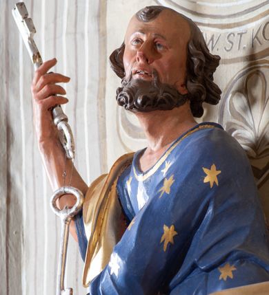 Zdjęcie nr 3: Figura ustawiona na niewielkiej podstawie. Zwrócona jest frontalnie, z uniesioną głową skierowaną w lewo, w kontrapoście, o esowato wygiętej sylwetce. Obie ręce wyciągnięte są w prawo, w lewej święty trzyma czerwoną księgę opartą na prawym udzie, w prawej, uniesionej w górę dłoni trzyma klucze. Twarz ma wychudzoną, o blisko siebie usytuowanych oczach, skierowanych do góry, prostym nosie, otwartych ustach z widocznymi zębami; okoloną krótką, silnie kręconą brodą oraz krótkimi, kręconymi włosami po bokach głowy i nad czołem, na głowie łysina. Święty ubrany jest w przylegającą do ciała niebieską tunikę o szerokich rękawach, z pozłacanymi lamówkami i wzorze z gwiazd. Pozłacany płaszcz jest diagonalnie przewiązany przez korpus, zarzucony na prawe ramię i opadający na prawy bok. Polichromia w partiach ciała naturalistyczna. 
