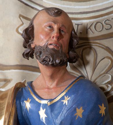Zdjęcie nr 11: Figura ustawiona na niewielkiej podstawie. Zwrócona jest frontalnie, z uniesioną głową skierowaną w lewo, w kontrapoście, o esowato wygiętej sylwetce. Obie ręce wyciągnięte są w prawo, w lewej święty trzyma czerwoną księgę opartą na prawym udzie, w prawej, uniesionej w górę dłoni trzyma klucze. Twarz ma wychudzoną, o blisko siebie usytuowanych oczach, skierowanych do góry, prostym nosie, otwartych ustach z widocznymi zębami; okoloną krótką, silnie kręconą brodą oraz krótkimi, kręconymi włosami po bokach głowy i nad czołem, na głowie łysina. Święty ubrany jest w przylegającą do ciała niebieską tunikę o szerokich rękawach, z pozłacanymi lamówkami i wzorze z gwiazd. Pozłacany płaszcz jest diagonalnie przewiązany przez korpus, zarzucony na prawe ramię i opadający na prawy bok. Polichromia w partiach ciała naturalistyczna. 
