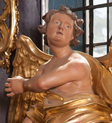 Zdjęcie nr 1: Dwie rzeźby aniołów ustawione są na niewielkich podstawach. Obie figury o układzie ciała w lustrzanym odbiciu względem siebie, zwrócone są frontalnie, w kontrapoście, z głowami skierowanymi w stronę pola głównego ołtarza oraz rękami wyciągniętymi w przeciwną stronę. Twarze mają pociągłe, o młodzieńczych rysach, blisko siebie osadzonych oczach, lekko garbatych nosach, rozchylonych ustach i wystających brodach, okolone ekspresyjnie rozwianymi, krótkimi włosami, rzeźbionymi w pojedyncze pasma. Anioły ubrane są w pozłocone, przylegające do ciała tuniki z jednym rękawem, odsłaniające część torsu i jedną nogę. Obie figury posiadają pozłocone, złożone skrzydła. Polichromia ciała naturalistyczna. 

