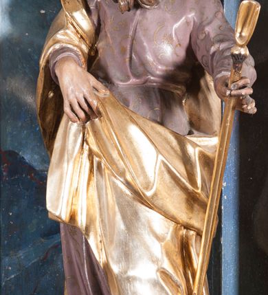 Zdjęcie nr 3: Rzeźba drążona z tyłu, ustawiona na niskiej podstawie z inskrypcją „S(anctus) Joachim”. Święty ukazany jest frontalnie, w kontrapoście, przechylony w lewo. Prawą ręką podtrzymuje z przodu połę płaszcza, w lewej, wyciągniętej w bok trzyma szuflę pasterską. Twarz ma pociągłą, o wysokim czole, prostym nosie, oczach osadzonych blisko siebie oraz rozchylonych pełnych ustach; okolona jest długą brodą opadającą na pierś oraz krótkimi, kręconymi włosami. Święty ubrany jest w jasnofioletową tunikę o pozłacanym wzorze i lamówce, przepasaną w talii oraz pozłacany płaszcz zawinięty na prawym ramieniu, otaczający postać i podtrzymywany z przodu prawą ręką. Polichromia ciała naturalistyczna. 
