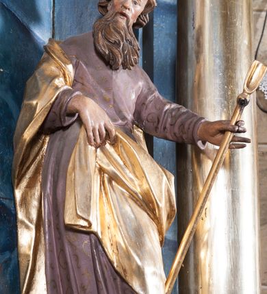 Zdjęcie nr 2: Rzeźba drążona z tyłu, ustawiona na niskiej podstawie z inskrypcją „S(anctus) Joachim”. Święty ukazany jest frontalnie, w kontrapoście, przechylony w lewo. Prawą ręką podtrzymuje z przodu połę płaszcza, w lewej, wyciągniętej w bok trzyma szuflę pasterską. Twarz ma pociągłą, o wysokim czole, prostym nosie, oczach osadzonych blisko siebie oraz rozchylonych pełnych ustach; okolona jest długą brodą opadającą na pierś oraz krótkimi, kręconymi włosami. Święty ubrany jest w jasnofioletową tunikę o pozłacanym wzorze i lamówce, przepasaną w talii oraz pozłacany płaszcz zawinięty na prawym ramieniu, otaczający postać i podtrzymywany z przodu prawą ręką. Polichromia ciała naturalistyczna. 
