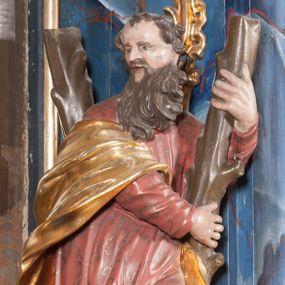 Zdjęcie nr 1: Rzeźba drążona z tyłu, ustawiona na niskiej podstawie. Święty ukazany frontalnie, z lewą nogą opartą na skale, o silnie skręconym w lewo korpusie i głowie skierowanej w przeciwną stronę. Obiema rękami obejmuje ramię stojącego za nim krzyża w kształcie litery „X”. Twarz ma pociągłą, o wysokim czole, lekko garbatym nosie, blisko siebie osadzonych oczach i pełnych, rozchylonych ustach; okolona jest długą, skręconą w pukle brodą, opadającą na pierś oraz krótkimi, kręconymi włosami. Święty ubrany jest w pomarańczowo-różową tunikę o pozłacanym wzorze, przepasaną w talii oraz pozłocony płaszcz przewiązany przez prawe przedramię i opadający na lewą nogę. Polichromia ciała w kolorze naturalistycznym. Na podstawie figury inskrypcja „S(anctus) Andreas”. 
