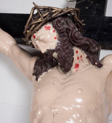 Zdjęcie nr 6: Figura umarłego Chrystusa jest przybita do krzyża o prostych ramionach trzema gwoździami. Ciało w dużym zwisie, o układzie ramion przyjmujących kształt litery „V” oraz dłoniach w geście błogosławieństwa. Głowa opada bezwładnie na prawy bark. Nogi są ugięte w kolanach, a stopy skrzyżowane w układzie prawa na lewą. Twarz Chrystusa jest pociągła, o prostym nosie, zamkniętych oczach i uniesionych brwiach, okolona silnie kręconą brodą oraz kręconymi włosami opadającymi na ramiona. Na głowie korona cierniowa. Ciało silnie umięśnione o wyraźnie podkreślonych żebrach klatki piersiowej. Perizonium krótkie, zawieszone na sznurze, odsłaniające prawe biodro, ze zwisem tkaniny na prawym boku. Ciało polichromowane w kolorze naturalistycznym z zaznaczonymi śladami męki, korona cierniowa i perizonium pozłocone. Pionowa belka krzyża zwieńczona tabliczką z napisem „IN / RI”.
