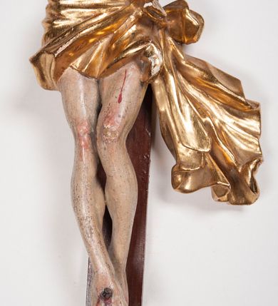 Zdjęcie nr 15: Figura umarłego Chrystusa przybita trzema gwoździami do prostego krzyża. Ciało o horyzontalnie rozłożonych ramionach, z głową opadającą na prawy bark, lewą nogą ugiętą w kolanie, prawą wyprostowaną oraz stopami skrzyżowanymi w układzie prawa na lewą. Twarz szczupła, z nosem o ostrym profilu, zamkniętych oczach i rozchylonych ustach, okolona jest rozdwajającą się brodą oraz silnie kręconymi włosami opadającymi na plecy i na prawe ramię. Na głowie szeroka korona cierniowa. Ciało szczupłe, smukłe, miękko modelowane, o podkreślonej muskulaturze ramion i ud oraz zaznaczonych delikatnie żebrach i mostku klatki piersiowej. Perizonium krótkie, silnie drapowane, zawiązane na sznurze, odsłaniające fragment lewego biodra z silnie rozwianym zwisem tkaniny na lewym boku. Polichromia ciała w kolorze naturalistycznym z zaznaczonymi śladami męki, korona cierniowa i perizonium pozłocone. Na zakończeniu pionowej belki krzyża banderola z napisem „I.N. / R.I.”

