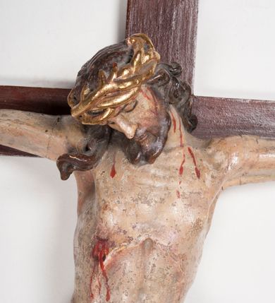 Zdjęcie nr 3: Figura umarłego Chrystusa przybita trzema gwoździami do prostego krzyża. Ciało o horyzontalnie rozłożonych ramionach, z głową opadającą na prawy bark, lewą nogą ugiętą w kolanie, prawą wyprostowaną oraz stopami skrzyżowanymi w układzie prawa na lewą. Twarz szczupła, z nosem o ostrym profilu, zamkniętych oczach i rozchylonych ustach, okolona jest rozdwajającą się brodą oraz silnie kręconymi włosami opadającymi na plecy i na prawe ramię. Na głowie szeroka korona cierniowa. Ciało szczupłe, smukłe, miękko modelowane, o podkreślonej muskulaturze ramion i ud oraz zaznaczonych delikatnie żebrach i mostku klatki piersiowej. Perizonium krótkie, silnie drapowane, zawiązane na sznurze, odsłaniające fragment lewego biodra z silnie rozwianym zwisem tkaniny na lewym boku. Polichromia ciała w kolorze naturalistycznym z zaznaczonymi śladami męki, korona cierniowa i perizonium pozłocone. Na zakończeniu pionowej belki krzyża banderola z napisem „I.N. / R.I.”

