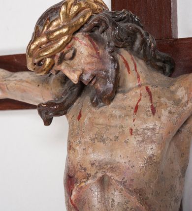 Zdjęcie nr 10: Figura umarłego Chrystusa przybita trzema gwoździami do prostego krzyża. Ciało o horyzontalnie rozłożonych ramionach, z głową opadającą na prawy bark, lewą nogą ugiętą w kolanie, prawą wyprostowaną oraz stopami skrzyżowanymi w układzie prawa na lewą. Twarz szczupła, z nosem o ostrym profilu, zamkniętych oczach i rozchylonych ustach, okolona jest rozdwajającą się brodą oraz silnie kręconymi włosami opadającymi na plecy i na prawe ramię. Na głowie szeroka korona cierniowa. Ciało szczupłe, smukłe, miękko modelowane, o podkreślonej muskulaturze ramion i ud oraz zaznaczonych delikatnie żebrach i mostku klatki piersiowej. Perizonium krótkie, silnie drapowane, zawiązane na sznurze, odsłaniające fragment lewego biodra z silnie rozwianym zwisem tkaniny na lewym boku. Polichromia ciała w kolorze naturalistycznym z zaznaczonymi śladami męki, korona cierniowa i perizonium pozłocone. Na zakończeniu pionowej belki krzyża banderola z napisem „I.N. / R.I.”

