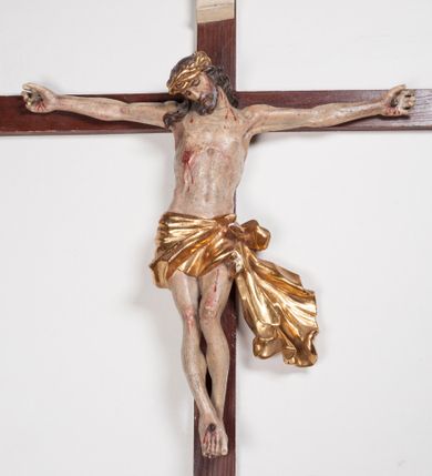 Zdjęcie nr 1: Figura umarłego Chrystusa przybita trzema gwoździami do prostego krzyża. Ciało o horyzontalnie rozłożonych ramionach, z głową opadającą na prawy bark, lewą nogą ugiętą w kolanie, prawą wyprostowaną oraz stopami skrzyżowanymi w układzie prawa na lewą. Twarz szczupła, z nosem o ostrym profilu, zamkniętych oczach i rozchylonych ustach, okolona jest rozdwajającą się brodą oraz silnie kręconymi włosami opadającymi na plecy i na prawe ramię. Na głowie szeroka korona cierniowa. Ciało szczupłe, smukłe, miękko modelowane, o podkreślonej muskulaturze ramion i ud oraz zaznaczonych delikatnie żebrach i mostku klatki piersiowej. Perizonium krótkie, silnie drapowane, zawiązane na sznurze, odsłaniające fragment lewego biodra z silnie rozwianym zwisem tkaniny na lewym boku. Polichromia ciała w kolorze naturalistycznym z zaznaczonymi śladami męki, korona cierniowa i perizonium pozłocone. Na zakończeniu pionowej belki krzyża banderola z napisem „I.N. / R.I.”


