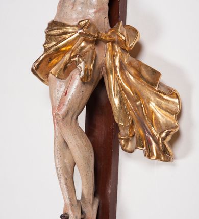 Zdjęcie nr 13: Figura umarłego Chrystusa przybita trzema gwoździami do prostego krzyża. Ciało o horyzontalnie rozłożonych ramionach, z głową opadającą na prawy bark, lewą nogą ugiętą w kolanie, prawą wyprostowaną oraz stopami skrzyżowanymi w układzie prawa na lewą. Twarz szczupła, z nosem o ostrym profilu, zamkniętych oczach i rozchylonych ustach, okolona jest rozdwajającą się brodą oraz silnie kręconymi włosami opadającymi na plecy i na prawe ramię. Na głowie szeroka korona cierniowa. Ciało szczupłe, smukłe, miękko modelowane, o podkreślonej muskulaturze ramion i ud oraz zaznaczonych delikatnie żebrach i mostku klatki piersiowej. Perizonium krótkie, silnie drapowane, zawiązane na sznurze, odsłaniające fragment lewego biodra z silnie rozwianym zwisem tkaniny na lewym boku. Polichromia ciała w kolorze naturalistycznym z zaznaczonymi śladami męki, korona cierniowa i perizonium pozłocone. Na zakończeniu pionowej belki krzyża banderola z napisem „I.N. / R.I.”

