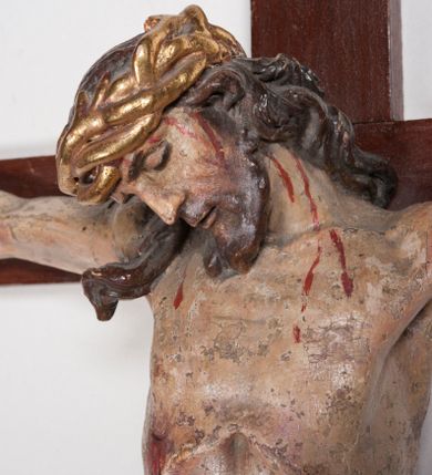 Zdjęcie nr 8: Figura umarłego Chrystusa przybita trzema gwoździami do prostego krzyża. Ciało o horyzontalnie rozłożonych ramionach, z głową opadającą na prawy bark, lewą nogą ugiętą w kolanie, prawą wyprostowaną oraz stopami skrzyżowanymi w układzie prawa na lewą. Twarz szczupła, z nosem o ostrym profilu, zamkniętych oczach i rozchylonych ustach, okolona jest rozdwajającą się brodą oraz silnie kręconymi włosami opadającymi na plecy i na prawe ramię. Na głowie szeroka korona cierniowa. Ciało szczupłe, smukłe, miękko modelowane, o podkreślonej muskulaturze ramion i ud oraz zaznaczonych delikatnie żebrach i mostku klatki piersiowej. Perizonium krótkie, silnie drapowane, zawiązane na sznurze, odsłaniające fragment lewego biodra z silnie rozwianym zwisem tkaniny na lewym boku. Polichromia ciała w kolorze naturalistycznym z zaznaczonymi śladami męki, korona cierniowa i perizonium pozłocone. Na zakończeniu pionowej belki krzyża banderola z napisem „I.N. / R.I.”


