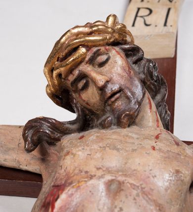 Zdjęcie nr 12: Figura umarłego Chrystusa przybita trzema gwoździami do prostego krzyża. Ciało o horyzontalnie rozłożonych ramionach, z głową opadającą na prawy bark, lewą nogą ugiętą w kolanie, prawą wyprostowaną oraz stopami skrzyżowanymi w układzie prawa na lewą. Twarz szczupła, z nosem o ostrym profilu, zamkniętych oczach i rozchylonych ustach, okolona jest rozdwajającą się brodą oraz silnie kręconymi włosami opadającymi na plecy i na prawe ramię. Na głowie szeroka korona cierniowa. Ciało szczupłe, smukłe, miękko modelowane, o podkreślonej muskulaturze ramion i ud oraz zaznaczonych delikatnie żebrach i mostku klatki piersiowej. Perizonium krótkie, silnie drapowane, zawiązane na sznurze, odsłaniające fragment lewego biodra z silnie rozwianym zwisem tkaniny na lewym boku. Polichromia ciała w kolorze naturalistycznym z zaznaczonymi śladami męki, korona cierniowa i perizonium pozłocone. Na zakończeniu pionowej belki krzyża banderola z napisem „I.N. / R.I.”

