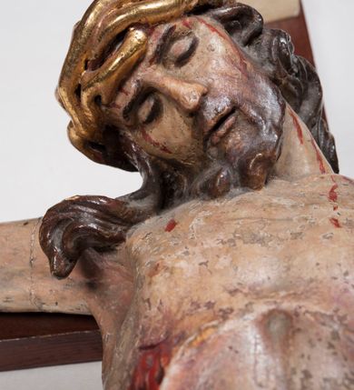 Zdjęcie nr 9: Figura umarłego Chrystusa przybita trzema gwoździami do prostego krzyża. Ciało o horyzontalnie rozłożonych ramionach, z głową opadającą na prawy bark, lewą nogą ugiętą w kolanie, prawą wyprostowaną oraz stopami skrzyżowanymi w układzie prawa na lewą. Twarz szczupła, z nosem o ostrym profilu, zamkniętych oczach i rozchylonych ustach, okolona jest rozdwajającą się brodą oraz silnie kręconymi włosami opadającymi na plecy i na prawe ramię. Na głowie szeroka korona cierniowa. Ciało szczupłe, smukłe, miękko modelowane, o podkreślonej muskulaturze ramion i ud oraz zaznaczonych delikatnie żebrach i mostku klatki piersiowej. Perizonium krótkie, silnie drapowane, zawiązane na sznurze, odsłaniające fragment lewego biodra z silnie rozwianym zwisem tkaniny na lewym boku. Polichromia ciała w kolorze naturalistycznym z zaznaczonymi śladami męki, korona cierniowa i perizonium pozłocone. Na zakończeniu pionowej belki krzyża banderola z napisem „I.N. / R.I.”


