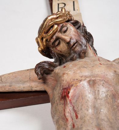 Zdjęcie nr 4: Figura umarłego Chrystusa przybita trzema gwoździami do prostego krzyża. Ciało o horyzontalnie rozłożonych ramionach, z głową opadającą na prawy bark, lewą nogą ugiętą w kolanie, prawą wyprostowaną oraz stopami skrzyżowanymi w układzie prawa na lewą. Twarz szczupła, z nosem o ostrym profilu, zamkniętych oczach i rozchylonych ustach, okolona jest rozdwajającą się brodą oraz silnie kręconymi włosami opadającymi na plecy i na prawe ramię. Na głowie szeroka korona cierniowa. Ciało szczupłe, smukłe, miękko modelowane, o podkreślonej muskulaturze ramion i ud oraz zaznaczonych delikatnie żebrach i mostku klatki piersiowej. Perizonium krótkie, silnie drapowane, zawiązane na sznurze, odsłaniające fragment lewego biodra z silnie rozwianym zwisem tkaniny na lewym boku. Polichromia ciała w kolorze naturalistycznym z zaznaczonymi śladami męki, korona cierniowa i perizonium pozłocone. Na zakończeniu pionowej belki krzyża banderola z napisem „I.N. / R.I.”

