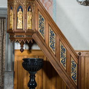 Zdjęcie nr 1: Ambona wisząca, przyścienna, z wejściem od prawej strony w postaci jednobiegowych schodów z balustradą, umieszczona  na północnej ścianie nawy. Kosz na rzucie części ośmioboku, poprzedzony od dołu partią cokołową o mniejszej średnicy, dekorowaną płycinami z ornamentem roślinnym. Dolna krawędź tej podstawy zdobiona maswerkami. Podwieszona do niej szyszka w formie wielokąta o przekroju ośmiobocznym. Ściany kosza dekorowane ostrołukowymi blendami, z płaskorzeźbionymi postaciami czterech ewangelistów; od lewej: Łukasz, Mateusz, Jan i Marek. Postacie są mocno wydłużone, każdy trzyma w rękach księgę, u stóp mają odpowiadające im symbole zwierzęce; każdy jest podpisany. W podłuczach arkadek ornament roślinny, powyżej pas rozetek. W balustradzie schodów romboidalne płyciny wypełnione esowato wygiętą wicią roślinną.
Struktura w kolorze bejcowanego na ciemno drewna; ornamenty, niektóre profile, szaty i atrybuty ewangelistów złocone; nisze malowane na granatowo.  