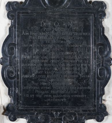 Zdjęcie nr 1: Płyta epitafijna w kształcie stojącego prostokąta o trzech bokach ujętych ramą kartuszową z esownicami spiętymi klamrą. W zwieńczeniu ramy medalion, zapewne na portret (niezachowany), powyżej krzyż trójlistny. W polu epitafium inskrypcja: "D(EO) O(PTIMO) M(AXIMO) / PIIS MANIBVS / AD(MODU)M R(EVERE)NDI OLIM M(AGNIFICI) BARTHOLOMAEI WIESIEWICZ / P(AROC)HIAE D(ICTAE) ECCLE(SI)AE HVIVS RECTORIS / ET PASTORIS / ZELO PIETATIS CVLTVS DIVINI, ET PROBITATIS VITAE / CONSPICVI. / CVIVS OPERA ET SVMPTV / FACIES HAEC, QVAE CONSPICITVR ECCLE(SI)AE, NOVV(M) / ET EXIMIVM SVMPSIT AVGMENTUM / AD PERPETVA(M) MEMORIA(M), VITA FELICITER FVNCTO / A(NNO) D(OMINI) 1693 DIE 18 MENIS IVLII / POST EXACTVM AETATIS SVAE / ANNORUV(M) LXXVIII CVRSUV(M) ET REGIMINIS ECCLE(SI)AE / SVPRA QVADRAGESIMVM / HOC  MNEMOSIINON / EXECVTORES STVDIO PIETATIS ACCENSI POSVERVNT / PRECARE REQVIEM VIATOR / SI ET TIBI PIVM ALIQVANDO, SVPEREST / DESIDERIVM".