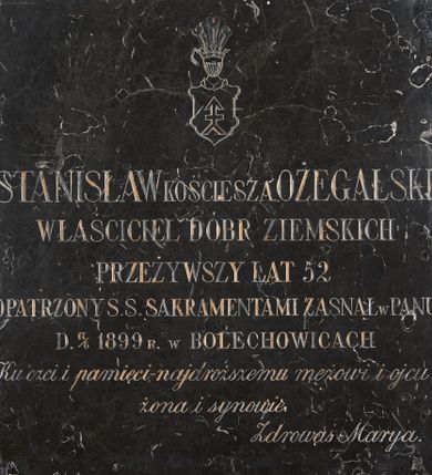 Zdjęcie nr 1: Kamienna płyta epitafijna w kształcie kwadratu. U góry wyryty herb Kościesza, poniżej inskrypcja: "STANISŁAW KOŚCIESZA OŻEGALSKI / WŁAŚCICIEL DÓBR ZIEMSKICH / PRZEŻYWSZY LAT 52 / OPATRZONY S.S. SAKRAMENTAMI ZASNĄŁ W PANU / D. 17/6 1899 R. W BOLECHOWICACH / Ku czci i pamięci - najdroższemu mężowi i ojcu - / żona i synowie. / Zdrowaś Marya."