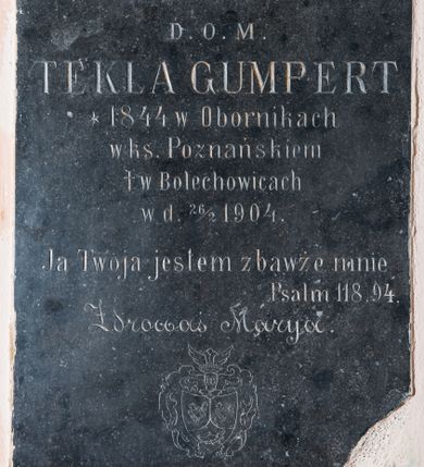 Zdjęcie nr 1: Tablica epitafijna kamienna w kształcie stojącego prostokąta z inskrypcją: „D(EO) O(PTIMO) M(AXIMO) / TEKLA GUMPERT / *1844 w Obornikach / w ks(ięstwie) Poznańskiem / + w Bolechowicach / w d(niu) 26/2 1904. / Ja Twoja jestem zbawże mnie / Psalm 118.94. / Zdrowaś Marya".
Poniżej napisu znajduje się herb rodziny Gumpertów (?). Tarcza gotycka przykryta hełmem prętowym z obfitymi labrami spływającymi do podstawy, zwieńczonym koroną otwartą, w której umieszczono klejnot w postaci dwóch skrzydeł z trzema kulami (?) pośrodku. Tarcza trójdzielna, w polach górnych powtórzone godło kogut, w polu dolnym trąba myśliwska. 
