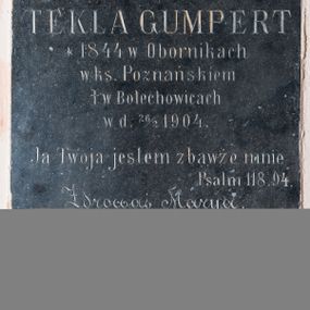 Zdjęcie nr 1: Tablica epitafijna kamienna w kształcie stojącego prostokąta z inskrypcją: „D(EO) O(PTIMO) M(AXIMO) / TEKLA GUMPERT / *1844 w Obornikach / w ks(ięstwie) Poznańskiem / + w Bolechowicach / w d(niu) 26/2 1904. / Ja Twoja jestem zbawże mnie / Psalm 118.94. / Zdrowaś Marya&quot;.
Poniżej napisu znajduje się herb rodziny Gumpertów (?). Tarcza gotycka przykryta hełmem prętowym z obfitymi labrami spływającymi do podstawy, zwieńczonym koroną otwartą, w której umieszczono klejnot w postaci dwóch skrzydeł z trzema kulami (?) pośrodku. Tarcza trójdzielna, w polach górnych powtórzone godło kogut, w polu dolnym trąba myśliwska. 