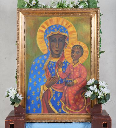 Zdjęcie nr 1: Feretron z obrazem w kształcie stojącego prostokąta z przedstawieniem Madonny z Dzieciątkiem w typie hodegetrii, wzorowanej na Matce Boskiej Częstochowskiej. Maria ukazana w półpostaci, frontalnie, na lewej ręce trzyma małego Jezusa, prawą na niego wskazuje . Ma pociągłą twarz, szeroko otwarte, ciemne oczy, wąski nos i małe usta. Dzieciątko prawą dłonią czyni gest błogosławieństwa, w lewej trzyma niewielką książkę. Maria jest ubrana w niebieską tunikę i  taki sam, podbity czerwienią płaszcz okrywający głowę i ramiona, Dzieciątko w długą czerwoną tunikę. Ubrania są lamowane złotem, szaty Marii dekorowane dodatkowo liliami, Dzieciątka drobnymi rozetkami. Wokół głów postaci cieniowane, żółtobrązowe okrągłe nimby. Formy potraktowano schematycznie i płasko. Tło niejednolite, nieokreślone, zielono-żółto-brązowe. Obraz ujęto profilowaną ramą.